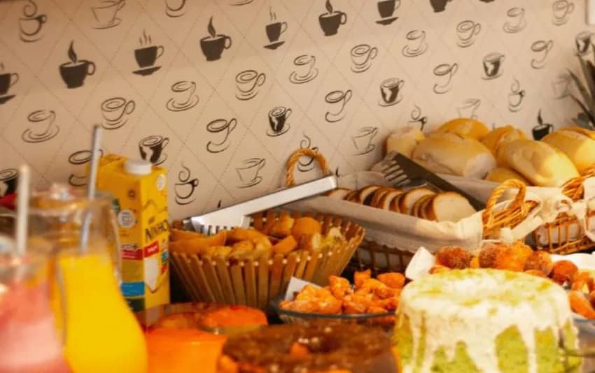 Foto de mesa com itens do café da manhã, incluindo pães, bolos, salgados e bebidas no Happy Hotel Brisa do Mar
