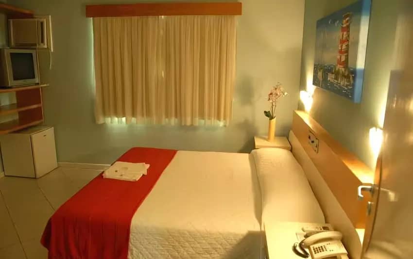 Foto de um quarto com cama de casal, janela ao fundo e frigobar no canto no Hotel Itália
